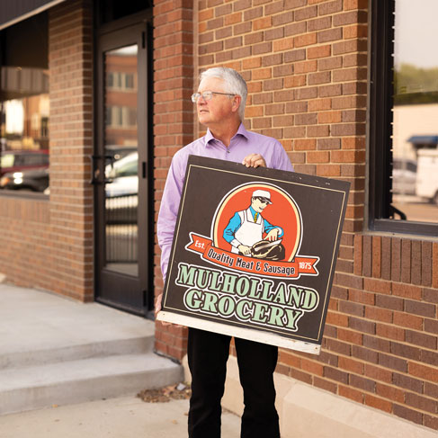 Tom Mulholland holding the Mulholland Grocery sign